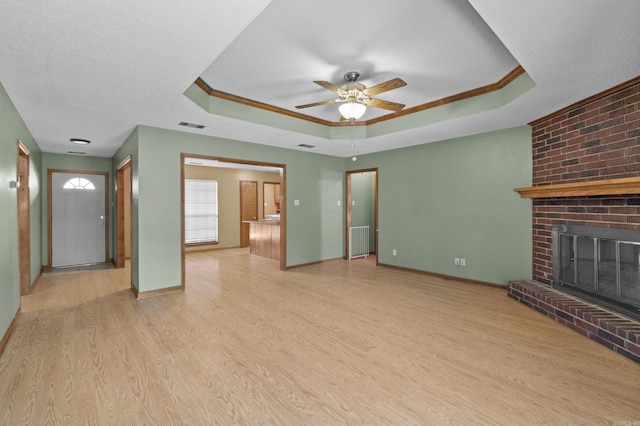 unfurnished living room featuring a tray ceiling, a brick fireplace, wood finished floors, and visible vents