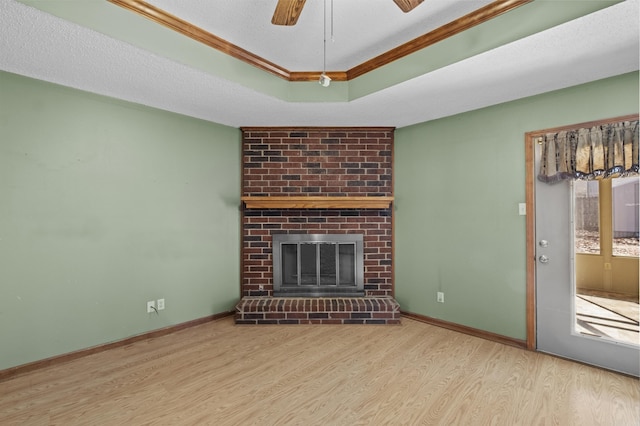 unfurnished living room with a textured ceiling, wood finished floors, baseboards, a brick fireplace, and a raised ceiling