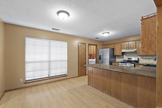 kitchen featuring under cabinet range hood, a peninsula, a sink, appliances with stainless steel finishes, and washer / clothes dryer