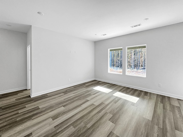 empty room with dark wood finished floors, visible vents, and baseboards