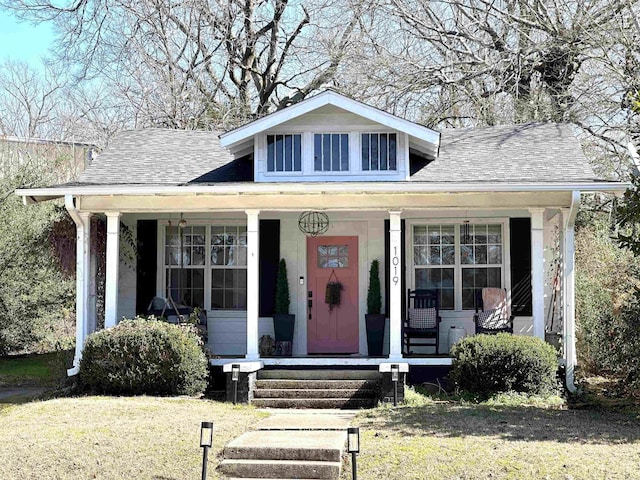 bungalow with covered porch, a front lawn, and roof with shingles