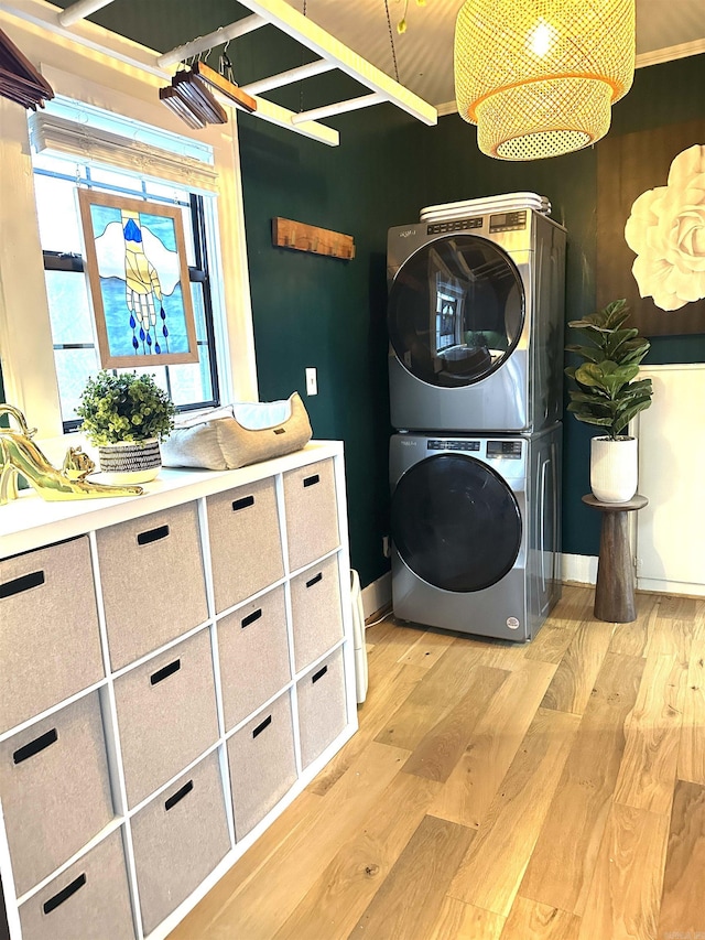 clothes washing area with baseboards, light wood finished floors, and stacked washer / drying machine