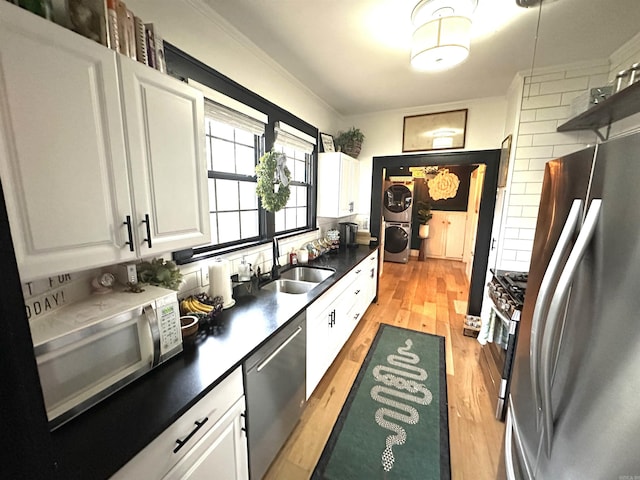 kitchen featuring stacked washer and dryer, light wood-style flooring, appliances with stainless steel finishes, white cabinetry, and a sink