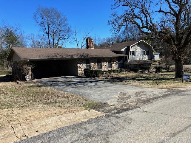 split level home with a garage, stone siding, aphalt driveway, and a chimney