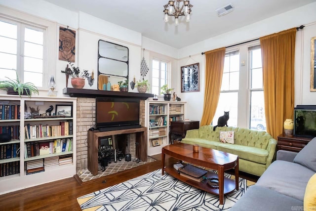 living area with a chandelier, a brick fireplace, visible vents, and wood finished floors