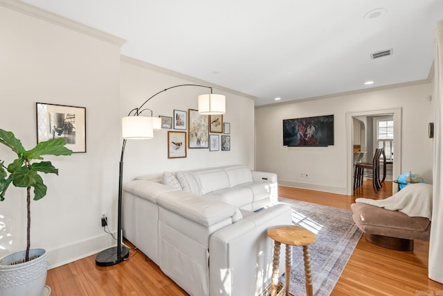 living room with baseboards, light wood-type flooring, visible vents, and crown molding