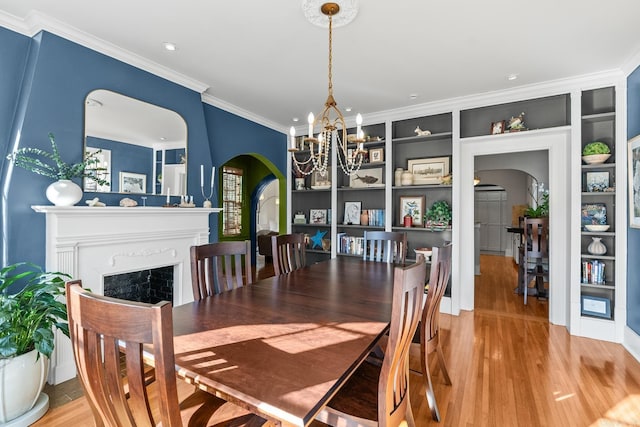 dining space with arched walkways, crown molding, a fireplace, an inviting chandelier, and light wood-type flooring