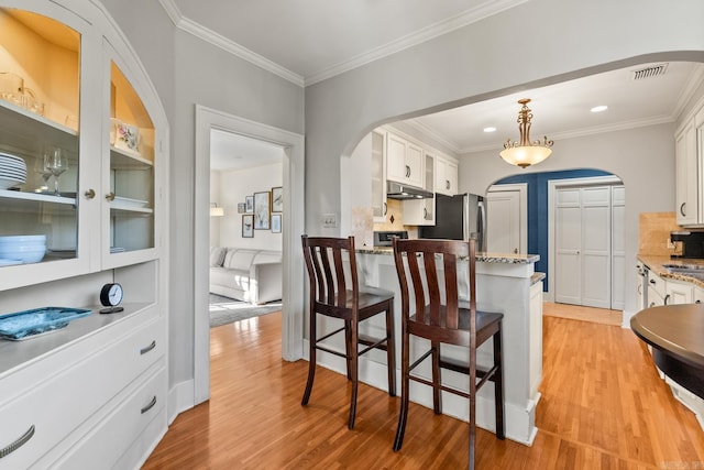 kitchen featuring light wood-type flooring, under cabinet range hood, white cabinetry, and arched walkways