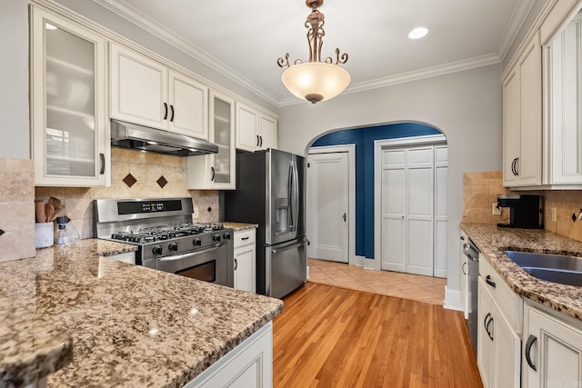 kitchen featuring stainless steel appliances, light wood-style flooring, ornamental molding, a sink, and under cabinet range hood