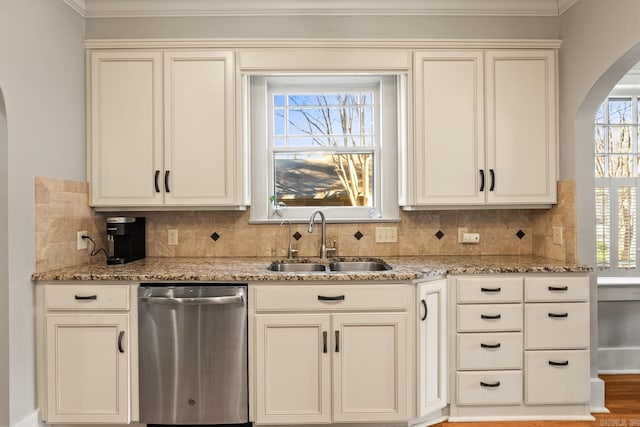 kitchen featuring arched walkways, light stone counters, backsplash, stainless steel dishwasher, and a sink