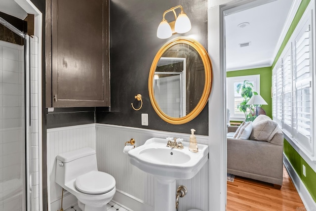 full bath with a wainscoted wall, crown molding, toilet, wood finished floors, and walk in shower