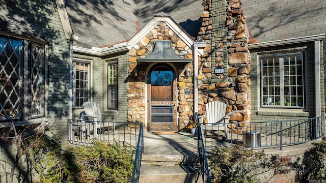 entrance to property featuring stone siding, brick siding, and roof with shingles