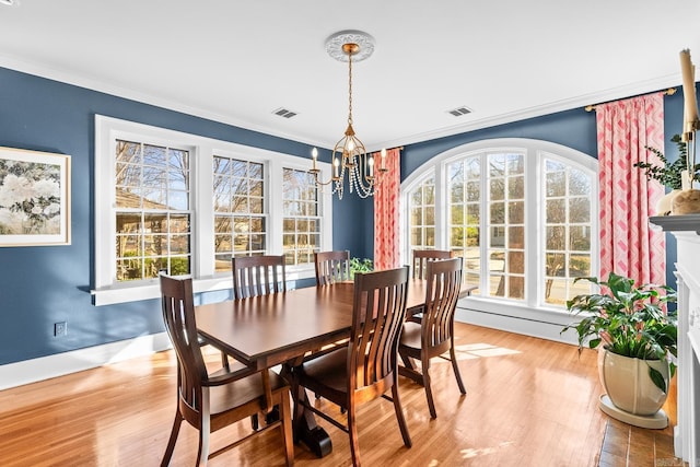 dining area featuring a fireplace, visible vents, light wood-style flooring, ornamental molding, and a chandelier