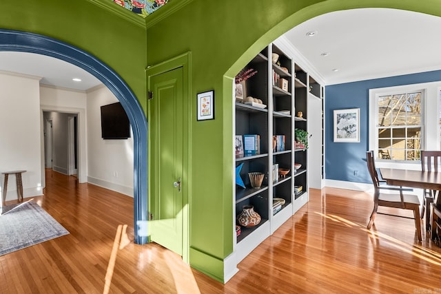 interior space with arched walkways, baseboards, wood finished floors, and crown molding