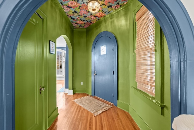 doorway with light wood-type flooring, baseboards, arched walkways, and ornamental molding