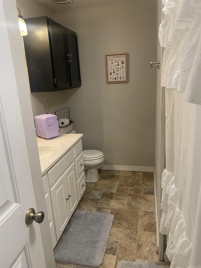 full bath featuring toilet, stone finish floor, vanity, and baseboards