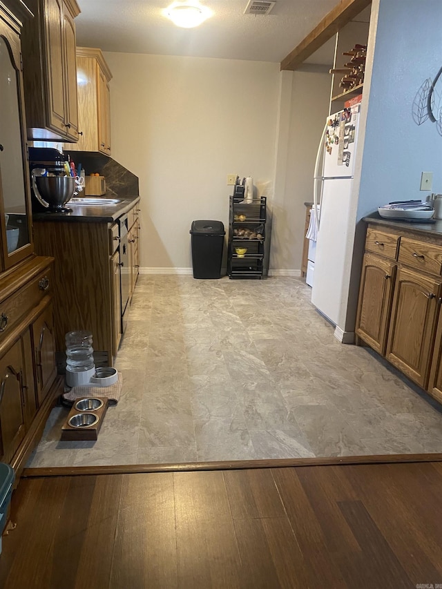 kitchen featuring visible vents, baseboards, freestanding refrigerator, light wood finished floors, and dark countertops