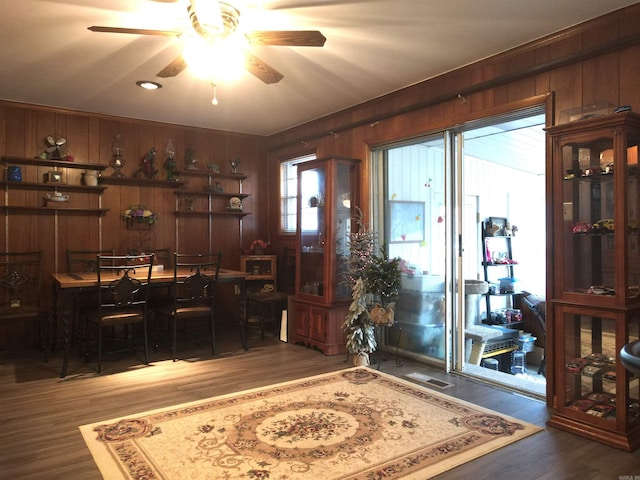 dining space featuring wood finished floors, wood walls, and a ceiling fan