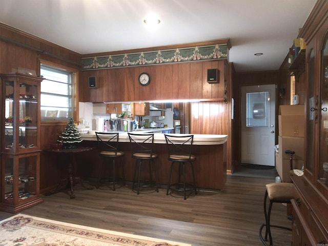 kitchen featuring a peninsula, brown cabinetry, wood finished floors, and under cabinet range hood