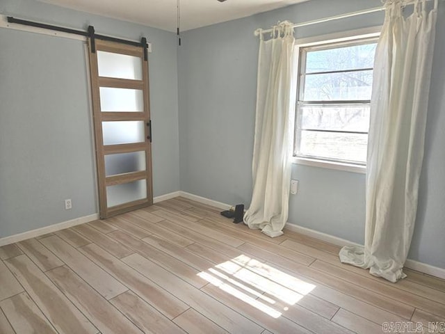 empty room with a wealth of natural light, a barn door, light wood-style flooring, and baseboards