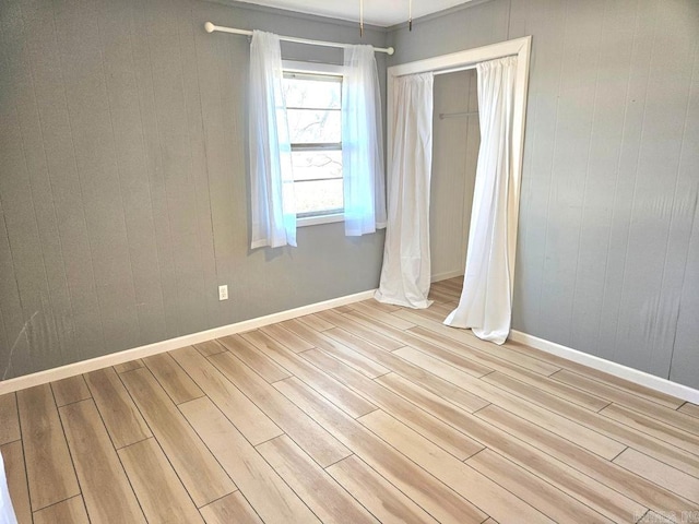 spare room featuring light wood finished floors, wood walls, and baseboards