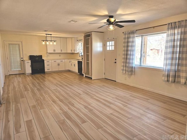 kitchen with white cabinets, hanging light fixtures, light countertops, black appliances, and light wood finished floors