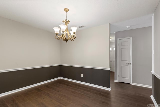 empty room featuring baseboards, wood finished floors, visible vents, and an inviting chandelier