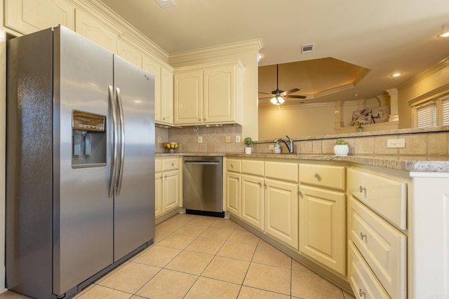 kitchen with light tile patterned flooring, ornamental molding, appliances with stainless steel finishes, backsplash, and a raised ceiling