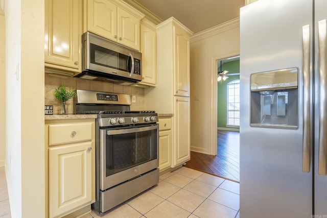 kitchen with light tile patterned floors, decorative backsplash, stainless steel appliances, cream cabinetry, and crown molding