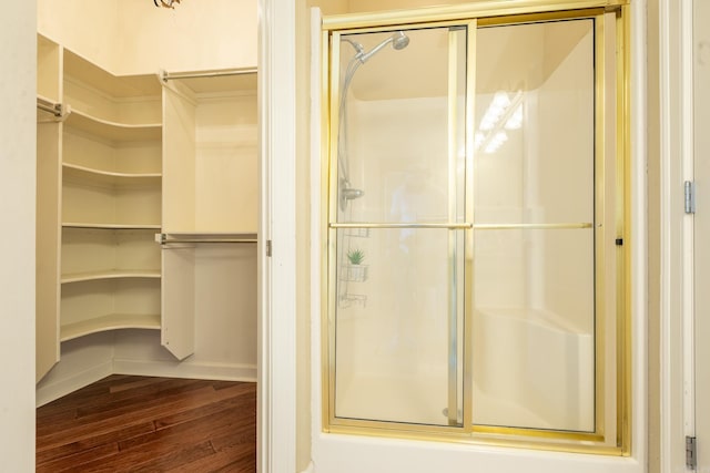 full bath featuring a stall shower, wood finished floors, a walk in closet, and baseboards