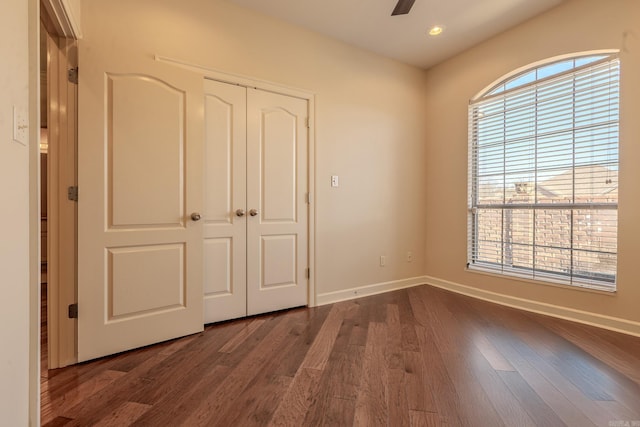 unfurnished bedroom featuring a closet, multiple windows, baseboards, and dark wood-type flooring