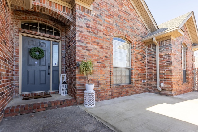 doorway to property with roof with shingles and brick siding