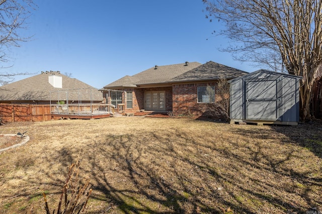 rear view of property featuring an outbuilding, brick siding, a storage unit, fence, and a deck