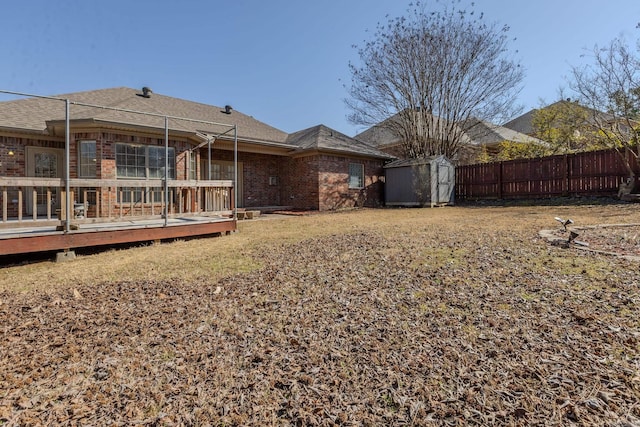 back of property featuring brick siding, fence, a deck, a shed, and an outdoor structure