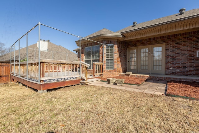 back of property with brick siding, a lawn, a wooden deck, and roof with shingles