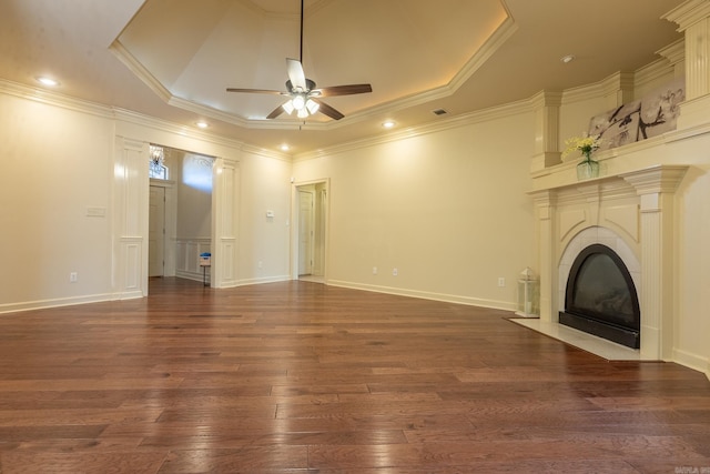 unfurnished living room featuring a tray ceiling, a fireplace, dark wood finished floors, ornamental molding, and ceiling fan