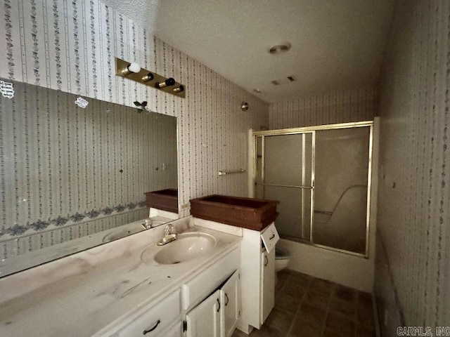 bathroom with bath / shower combo with glass door, toilet, vanity, tile patterned flooring, and wallpapered walls