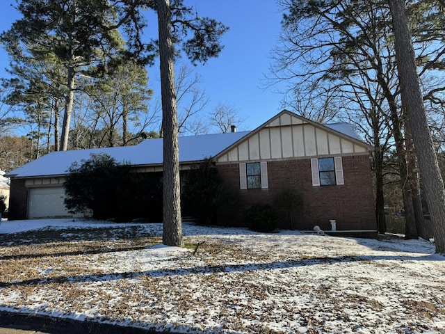 view of snowy exterior with brick siding, board and batten siding, and an attached garage