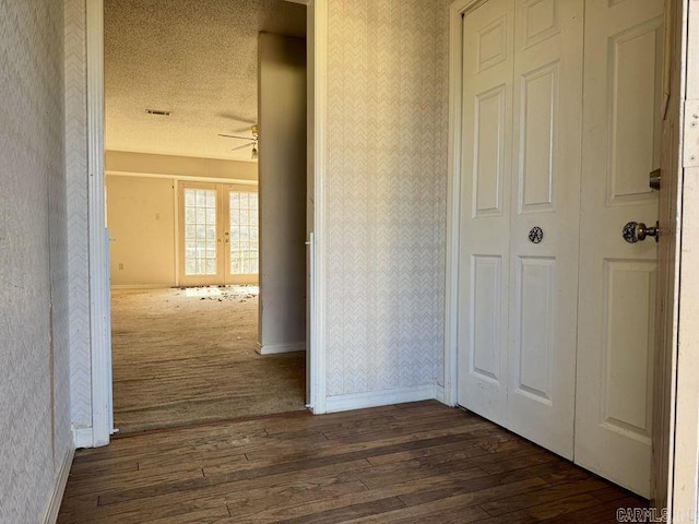 corridor with wallpapered walls, a textured ceiling, baseboards, and dark wood-type flooring