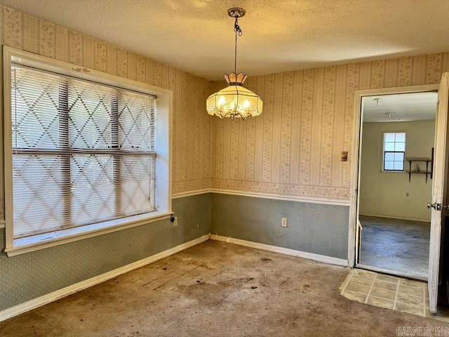 unfurnished dining area with wallpapered walls, carpet, a textured ceiling, and wainscoting