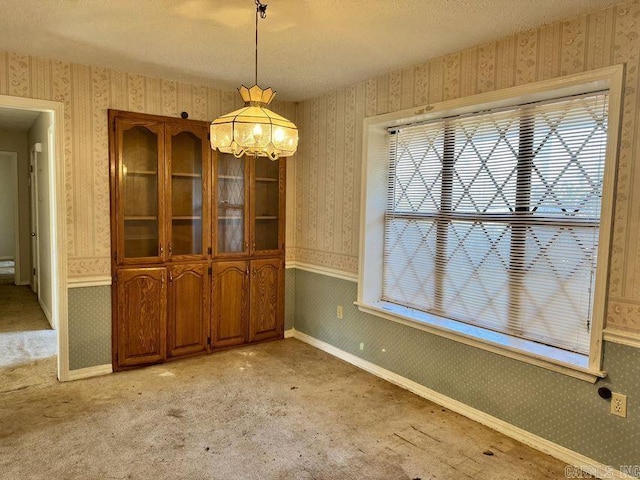 unfurnished dining area with a wainscoted wall, a textured ceiling, light carpet, and wallpapered walls