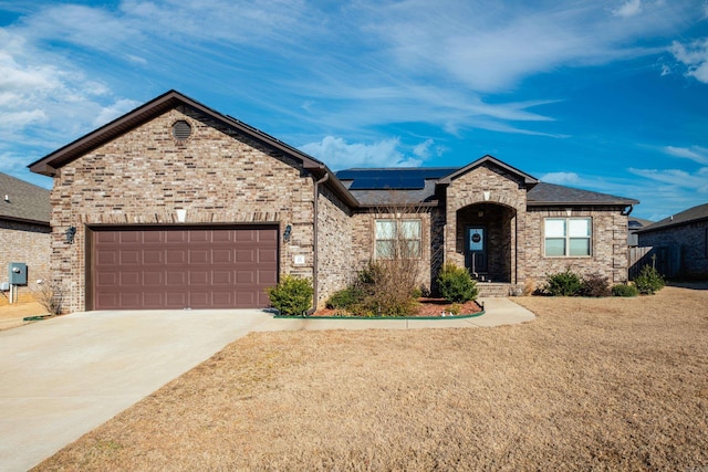 view of front of property featuring a garage, driveway, roof mounted solar panels, and brick siding