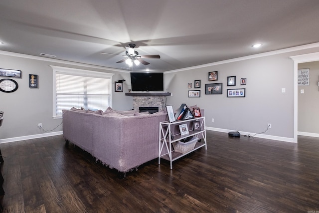 living room featuring ornamental molding, ceiling fan, a stone fireplace, wood finished floors, and baseboards