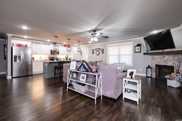 living room with a ceiling fan, ornamental molding, dark wood-type flooring, a fireplace, and recessed lighting