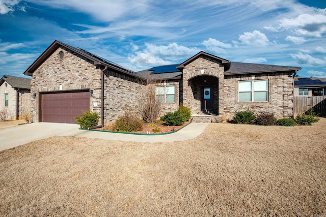 view of front of home featuring an attached garage, solar panels, brick siding, fence, and driveway