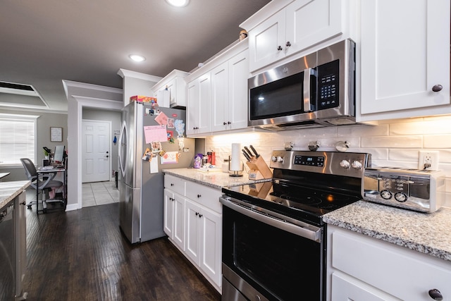 kitchen featuring dark wood-type flooring, white cabinetry, appliances with stainless steel finishes, light stone countertops, and tasteful backsplash