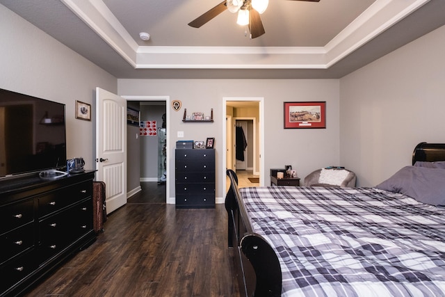 bedroom featuring a tray ceiling, dark wood-style flooring, a ceiling fan, and baseboards