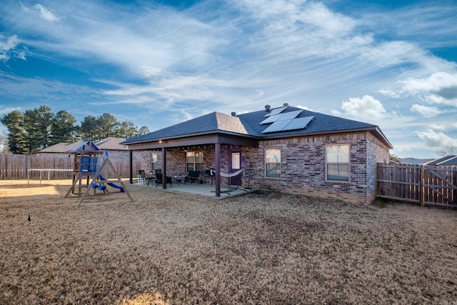 back of property with a playground, brick siding, roof mounted solar panels, a patio area, and a fenced backyard