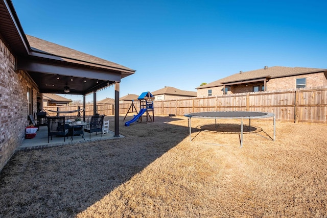 view of yard with a ceiling fan, a patio, a fenced backyard, a trampoline, and a playground