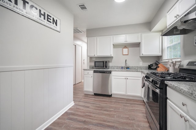 kitchen with appliances with stainless steel finishes, white cabinets, a sink, and under cabinet range hood